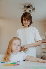 A mother lovingly braids her daughter's hair while they draw together, capturing a tender moment of family bonding and creative play. Perfect for parenting and lifestyle content