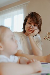 A mother lovingly braids her daughter's hair while they draw together, capturing a tender moment of family bonding and creative play. Perfect for parenting and lifestyle content