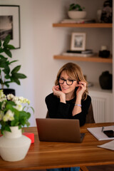 Blond haired middle-aged woman sitting at home and using her laptop