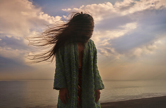 Man in chapan kaftan by the shore at sunset with windblown hair