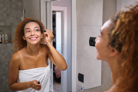 Woman applying mascara in bathroom mirror during morning routine