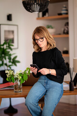 Blond haired confident woman sitting at desk at home and using her smartphone