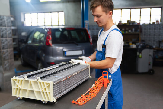 Serviceman replacing hybrid electric vehicle battery pack in workshop