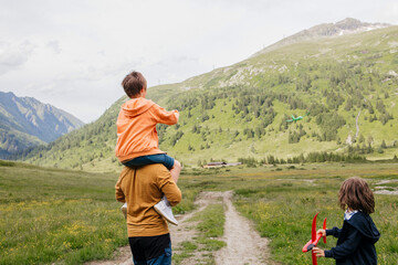 Boy with brother sitting on father's shoulder and spending leisure time on meadow