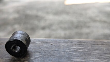 A horizontal shot of a small, worn, black rubber bushing or grommet resting on a weathered wooden...