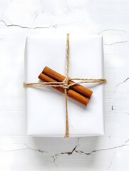 White gift box tied with twine and cinnamon sticks on a cracked white background