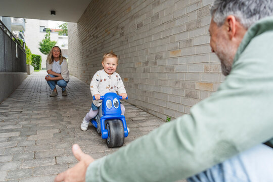Child riding toy vehicle outdoors with parents enjoying quality time