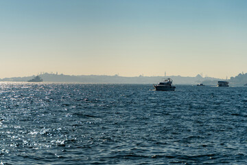 Scenic view of vessels navigating the sparkling waters of the Bosphorus, reflecting sunlight, with distant silhouettes of Istanbul coastline and mosques. Turkey travel concept
