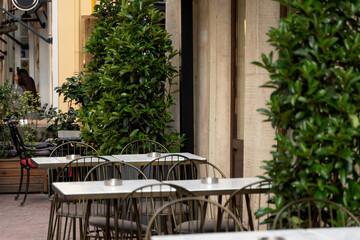 Empty tables and chairs in an outdoor cafe surrounded by vibrant greenery, inviting a peaceful moment, ideal for cafes, restaurants, outdoor dining, urban life, tourism, and lifestyle themes