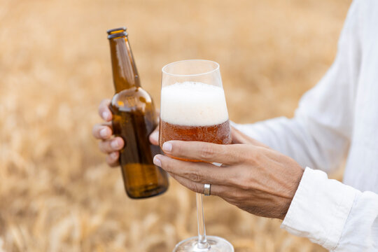 Hand holding beer glass and bottle in wheat field during summer