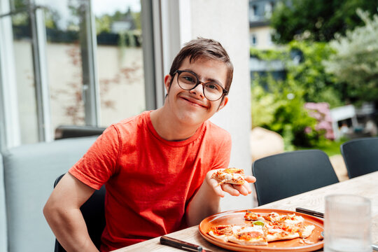 Smiling teenager with trisomy 21 enjoying pizza indoors