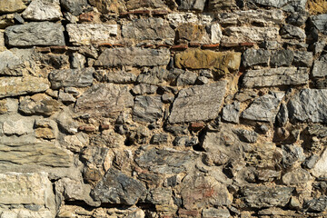 Fototapeta premium Textured stone wall features a variety of rock sizes and shapes, displaying natural colors and intricate patterns, perfect for use as backgrounds or architectural design elements in creative projects