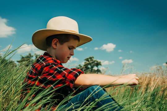 Cowboy schoolboy sitting on grass outdoors thinking under blue sky
