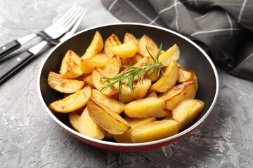 Tasty baked potatoes with rosemary in frying pan on grey textured table, closeup