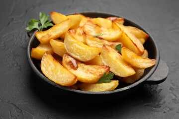 Tasty baked potatoes with parsley in frying pan on dark textured table, closeup