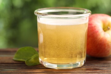 Delicious cider in glass, apple and green leaves on wooden table outdoors, closeup
