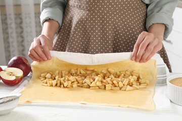 Woman making delicious apple strudel at white wooden table in kitchen, closeup