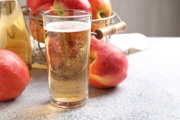 Delicious cider in glass, bottle and apples on light grey table, closeup. Space for text