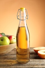 Delicious cider in glass bottle and apples on wooden table against orange gradient background