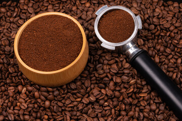 Holder with ground coffee on the background of roasted coffee beans with wooden cup. Coffee horn and coffee beans background texture.
