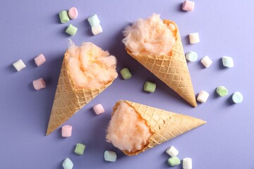 Cotton candy in waffle cones and marshmallows on violet background, flat lay