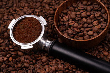 Holder with ground coffee on the background of roasted coffee beans with wooden cup. Coffee horn and coffee beans background texture.