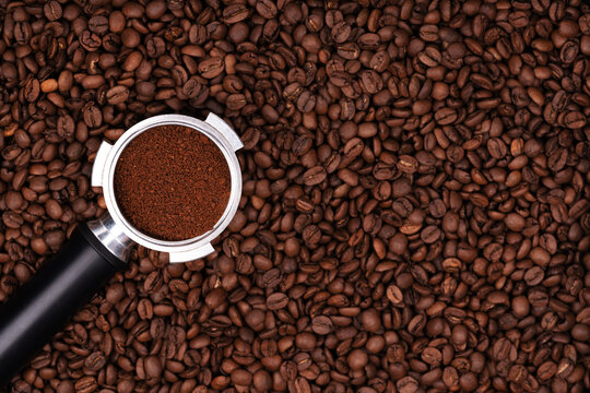 Holder with ground coffee on the background of roasted coffee beans. Coffee horn and coffee beans background texture.