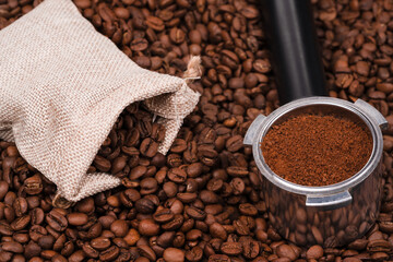 Jute bag and holder with ground coffee on the background of roasted coffee beans. coffee beans background texture.