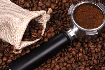 Jute bag and holder with ground coffee on the background of roasted coffee beans. coffee beans background texture.
