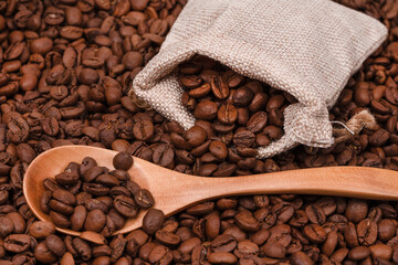 Jute bag with coffee beans and wooden spoon on the background of roasted coffee beans. coffee beans background texture.