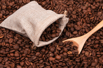 Jute bag with coffee beans and wooden spoon on the background of roasted coffee beans. coffee beans background texture.