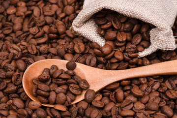 Jute bag with coffee beans and wooden spoon on the background of roasted coffee beans. coffee beans background texture.