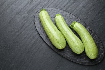 Fresh ripe zucchinis on black textured table, top view. Space for text