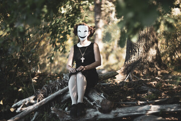 Masked schoolgirl in forest sitting quietly on autumn tree.