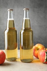 Delicious cider in glass bottles and apples on table against gray background