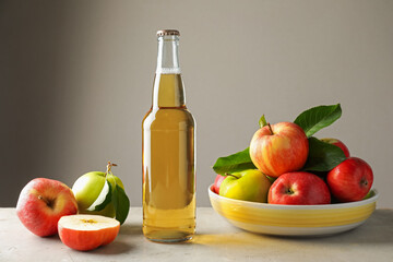 Delicious cider in glass bottle and apples on gray table against light background