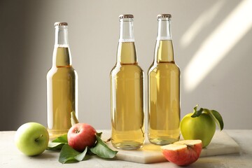Delicious cider in glass bottles and apples on gray table against light background
