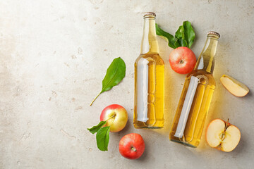 Delicious cider in glass bottles and apples on gray textured table, flat lay. Space for text