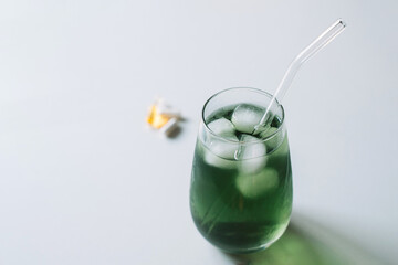 Angled top view of an iced chlorophyll drink with a glass straw, vitamins blurred in the background. Horizontal with copy space.