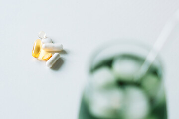 Vitamins in sharp focus, capsules, tablet, softgel, on a light surface, green drink blurred in the background. Horizontal with copy space.