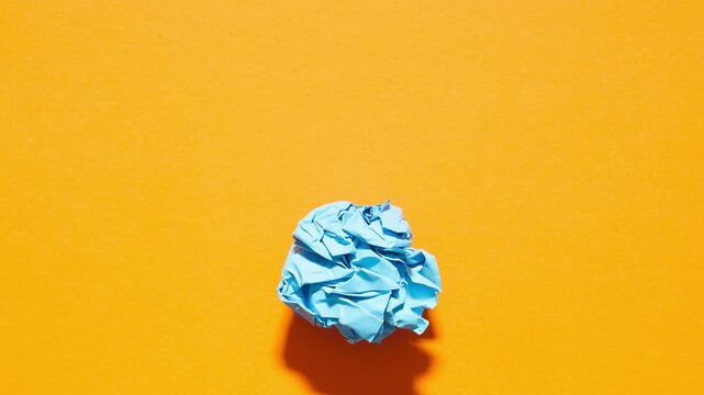 Blue crumpled paper unfolds on orange in a stop motion transition