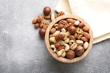 Mix of different nuts in bowl on grey textured table, top view. Space for text