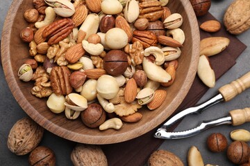 Mix of different nuts in bowl and nutcracker on grey table, flat lay