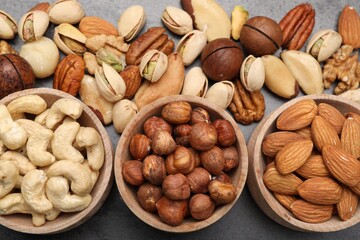 Mix of different nuts in bowls on grey table, flat lay