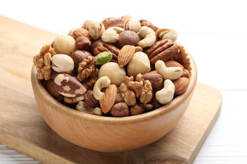 Mix of different nuts in bowl on white wooden table, closeup