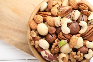 Mix of different nuts in bowl on white table, top view. Space for text