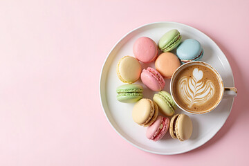 Multicolored French macarons on a plate, next to a cup of cappuccino with a pattern on a light pink background. Top view.