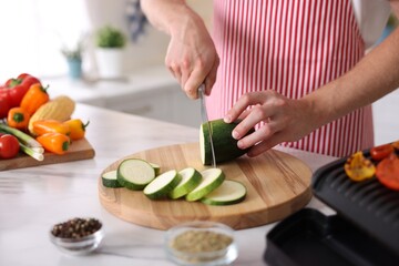 Man cutting zucchini at table in kitchen, closeup