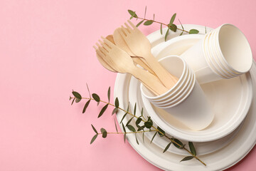 Set of disposable tableware and eucalyptus branches on pink background, top view. Space for text