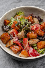 Fresh chicken salad with crispy fried pieces, lettuce, tomatoes, mixed greens, and dressing served in a ceramic bowl on gray background